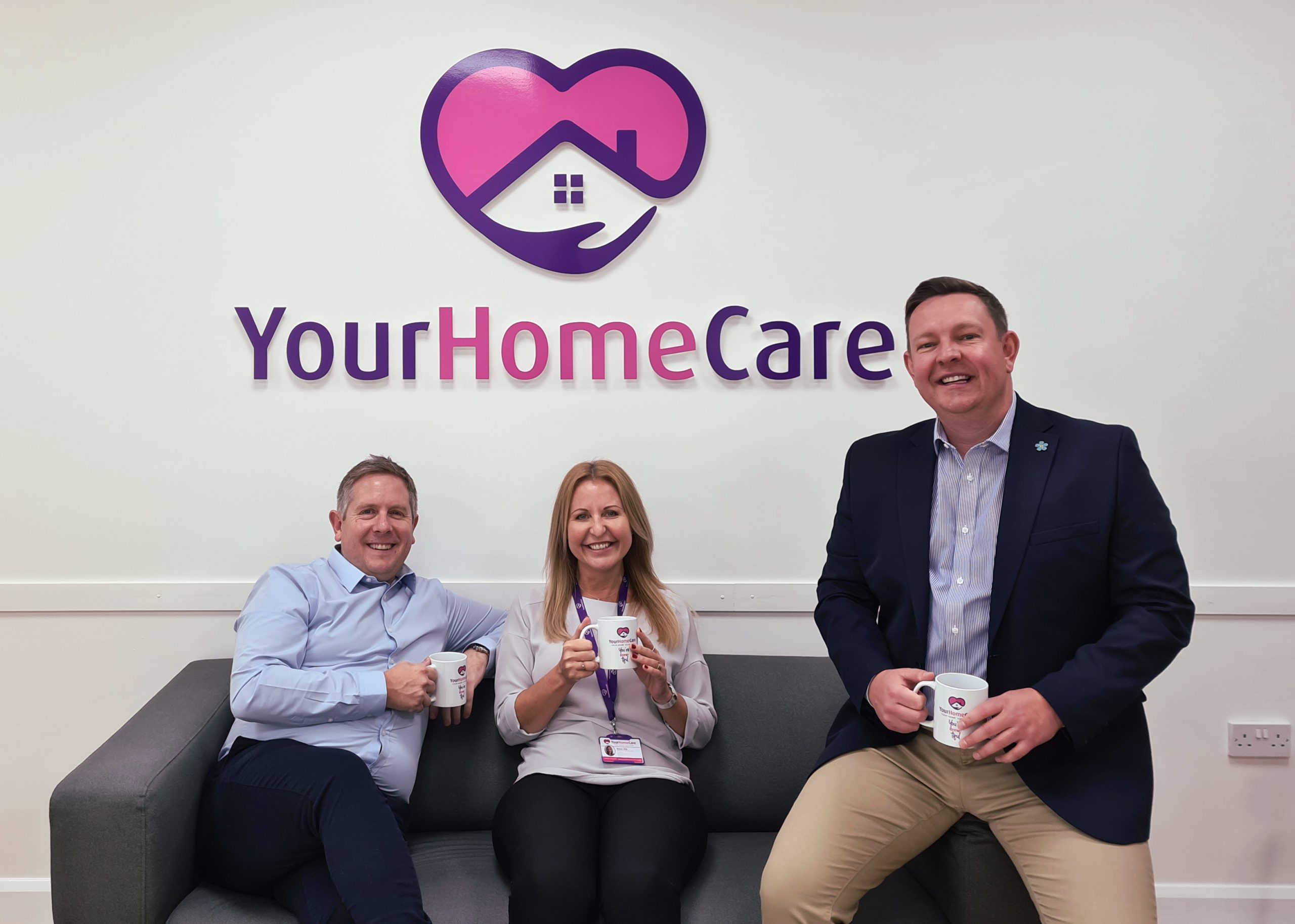 Paul Pitchford and Denise Pitts seated on a settee at Your Home Care, with Scott March seated on the end of the sofa, with the company logo in the background.