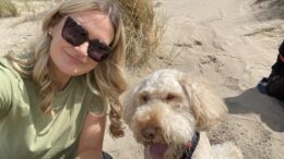 Picture shows a lady wearig sunglasses and to her left is a dog.