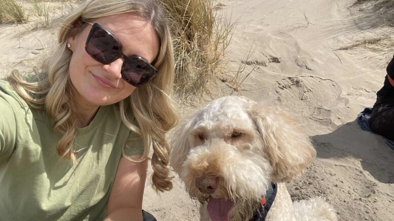 Picture shows a lady wearig sunglasses and to her left is a dog.